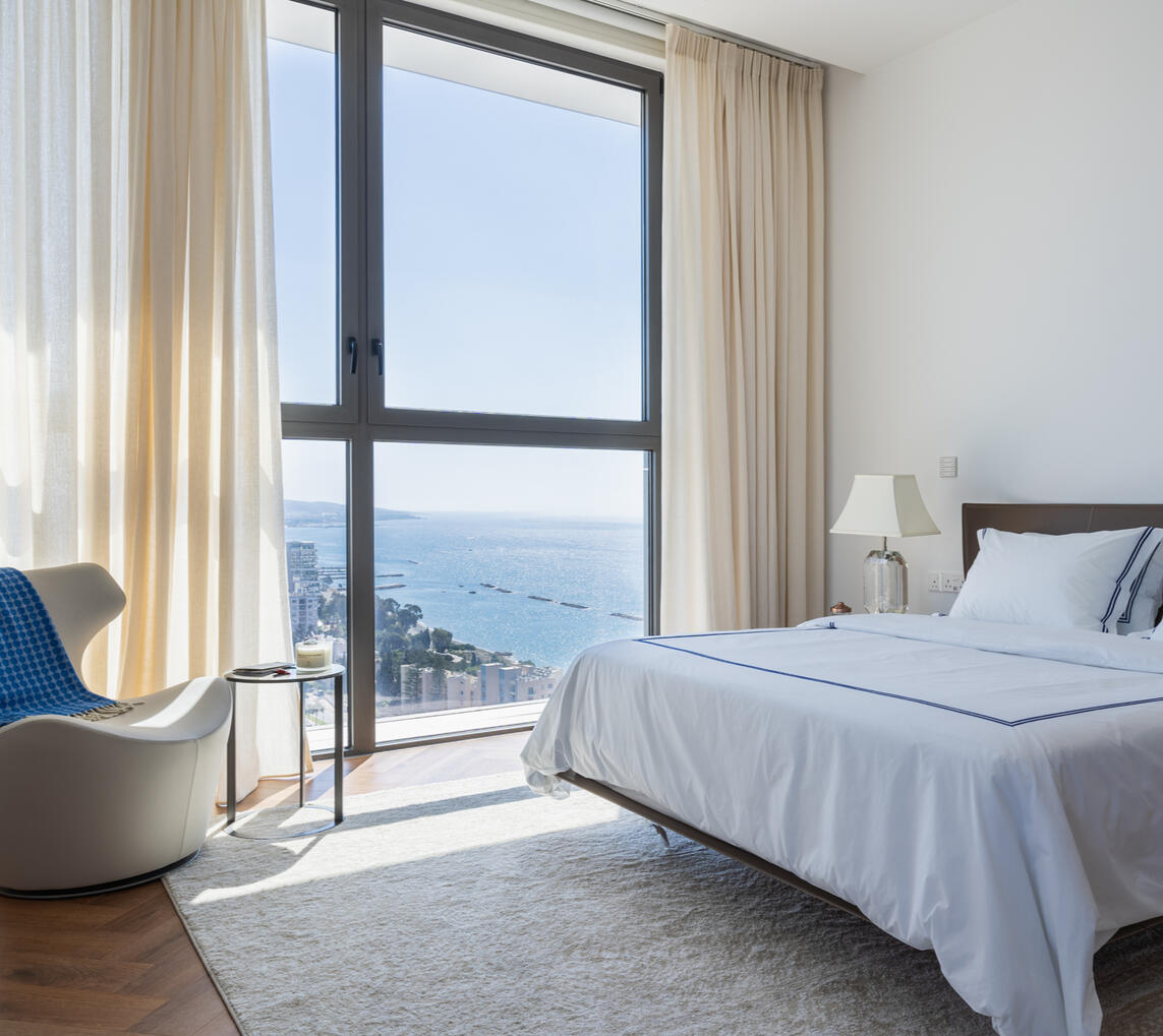 Luxury Bedroom with Panoramic Sea View in Limassol Interior photography of a modern bedroom with floor-to-ceiling windows and panoramic views of Limassol and the Mediterranean Sea.